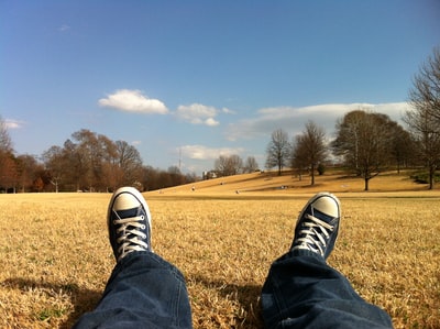 白天穿着蓝白匡威全明星鞋坐在棕色草地上拍照